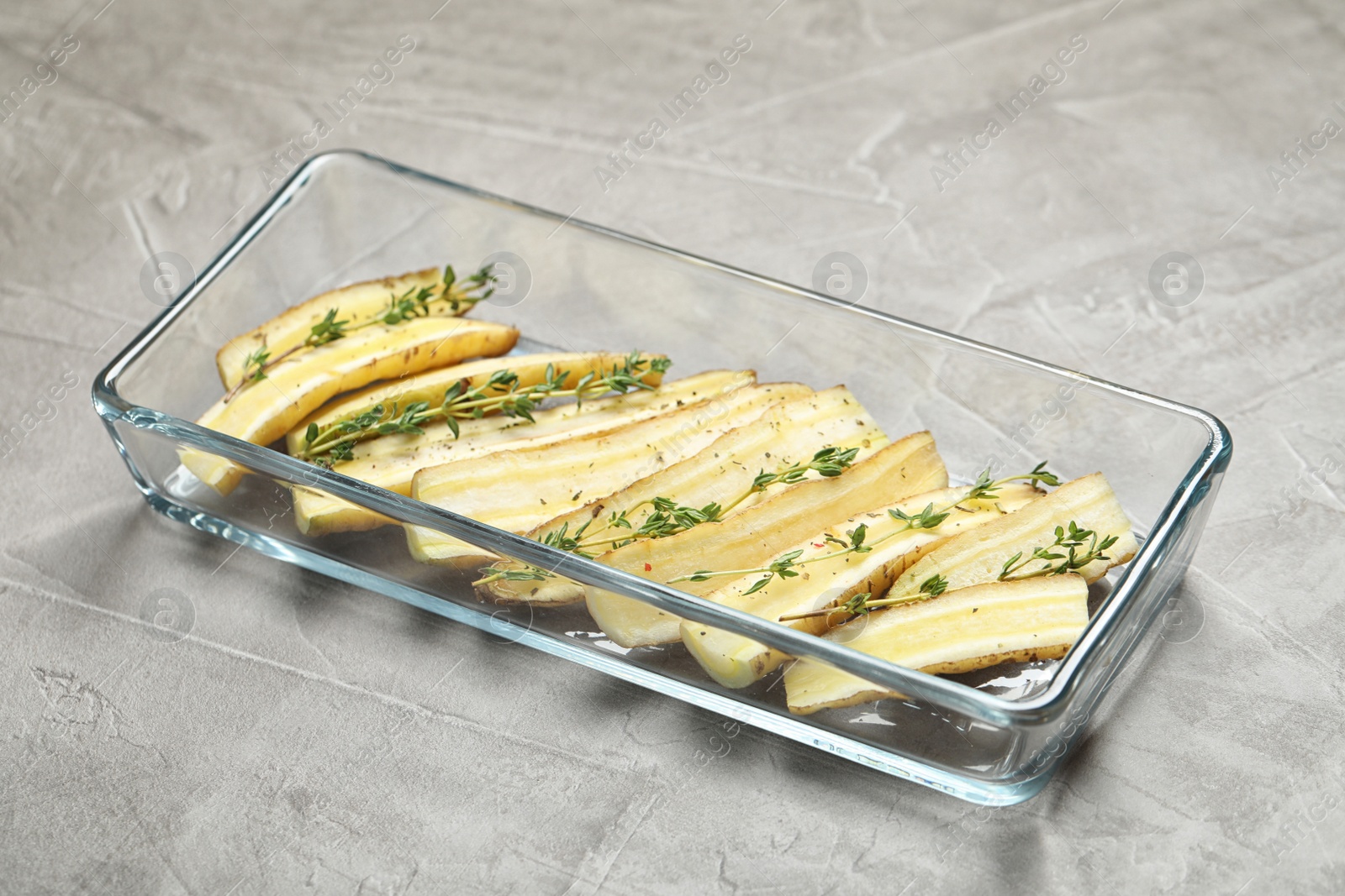 Photo of Raw cut white carrot with thyme in baking dish on light grey table, closeup