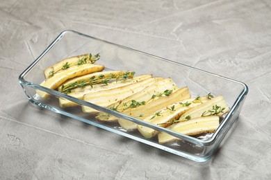 Photo of Raw cut white carrot with thyme in baking dish on light grey table, closeup