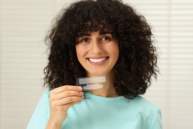 Young woman holding teeth whitening strips indoors