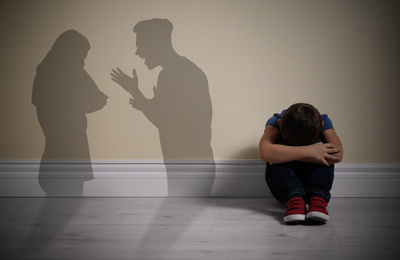 Little boy sitting on floor near yellow wall and silhouettes of arguing parents 