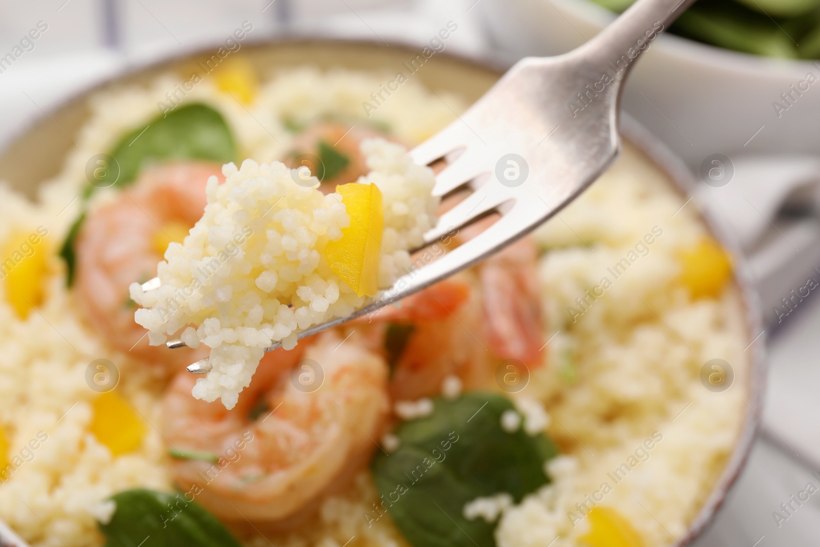 Photo of Fork with tasty couscous over plate, closeup