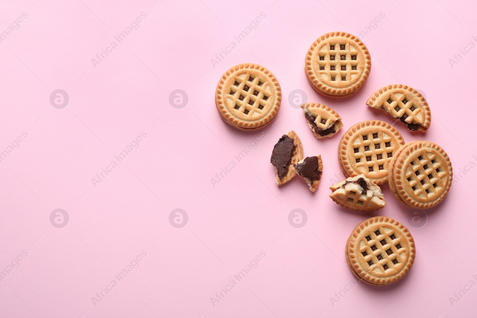 Photo of Tasty sandwich cookies with cream on pink background, flat lay. Space for text