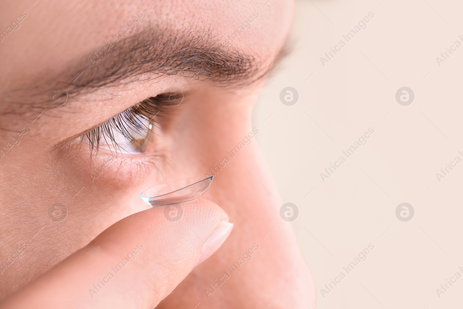 Photo of Young man putting contact lens in his eye, closeup