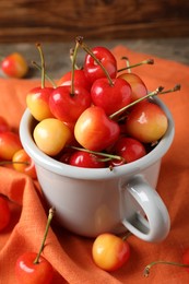 Photo of Sweet red cherries in mug on orange fabric