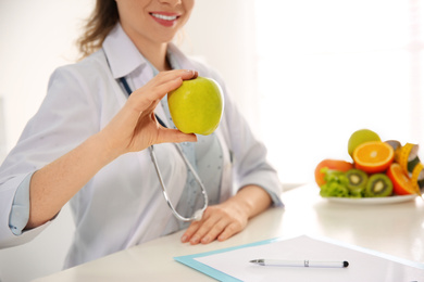 Photo of Nutritionist with apple at desk in office, closeup. Space for text