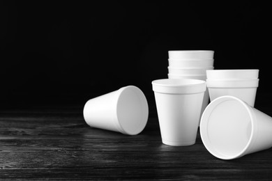 Photo of Many white styrofoam cups on black wooden table, space for text