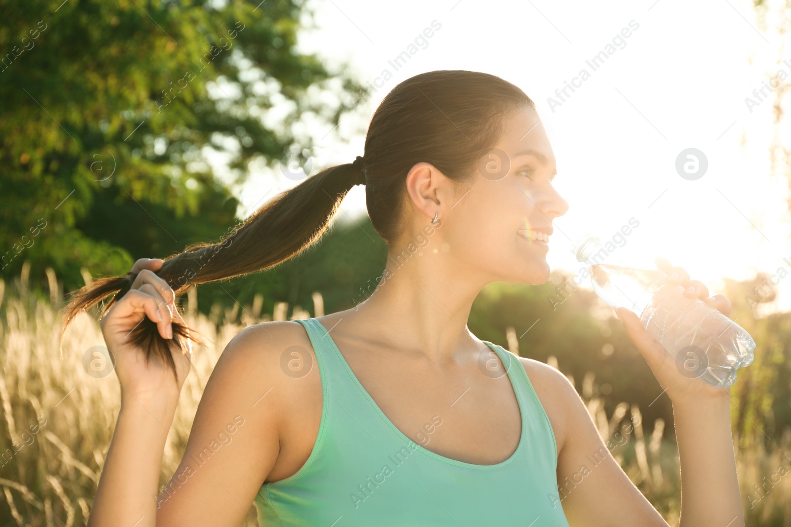 Photo of Happy young woman drinking water outdoors on hot summer day. Refreshing drink