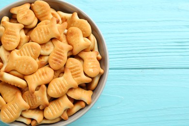 Delicious goldfish crackers in bowl on light blue wooden table, top view. Space for text