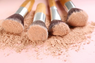 Different makeup brushes with crushed cosmetic product on pink background, closeup