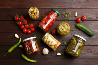 Jars of pickled vegetables and ingredients on wooden table, flat lay