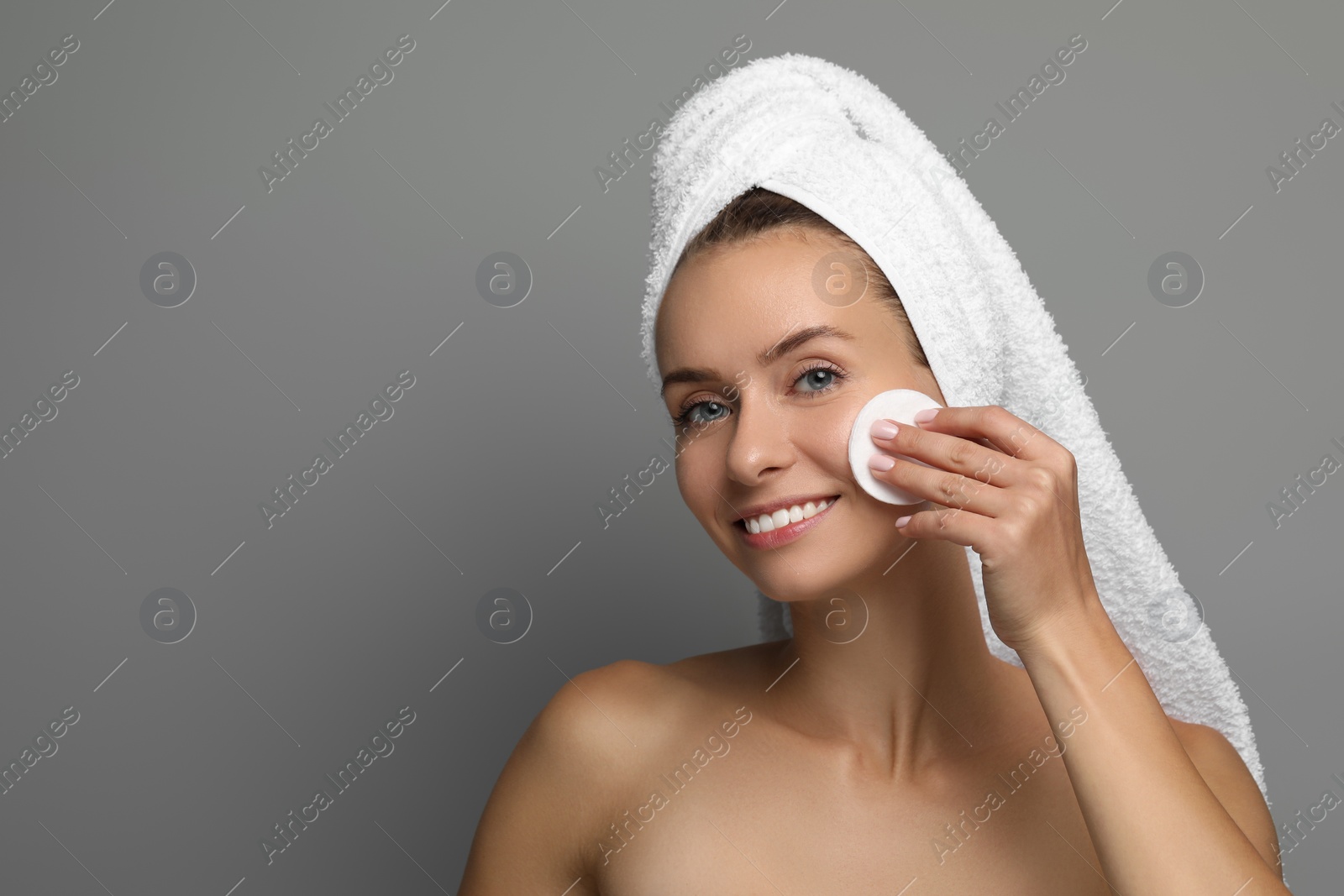 Photo of Smiling woman removing makeup with cotton pad on grey background. Space for text