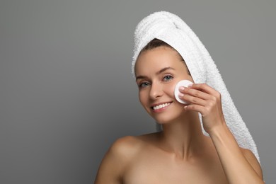 Smiling woman removing makeup with cotton pad on grey background. Space for text