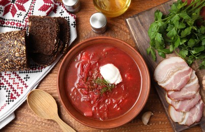 Clay bowl with Ukrainian borsch served on wooden table, flat lay