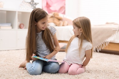 Photo of Cute little sisters reading book together at home