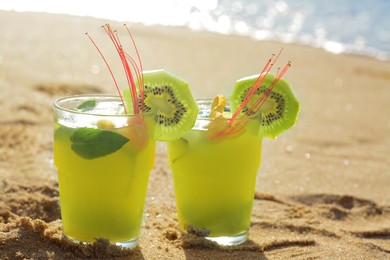 Photo of Glasses of refreshing drink with kiwi and mint on sand near sea