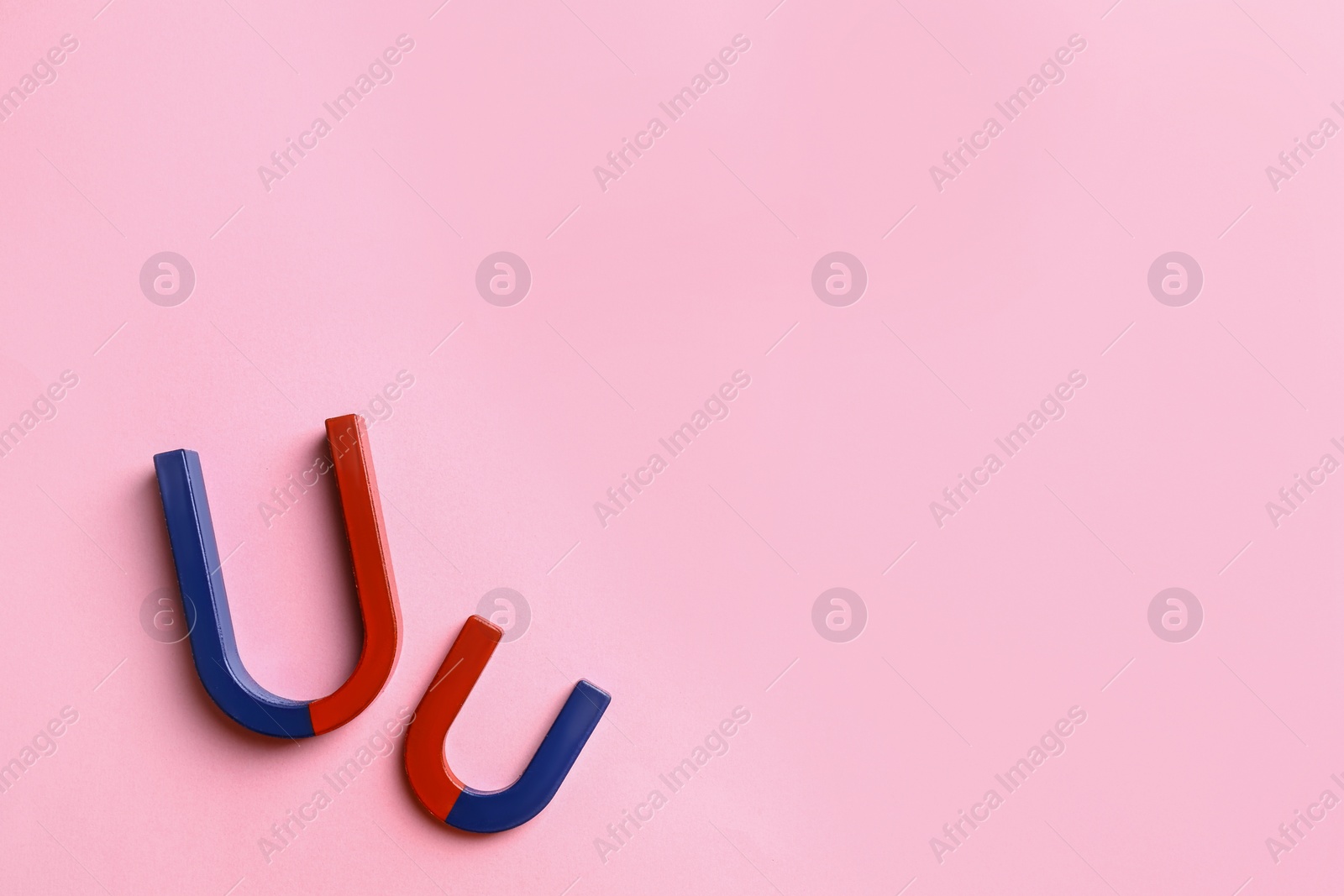 Photo of Red and blue horseshoe magnets on pink background, flat lay. Space for text