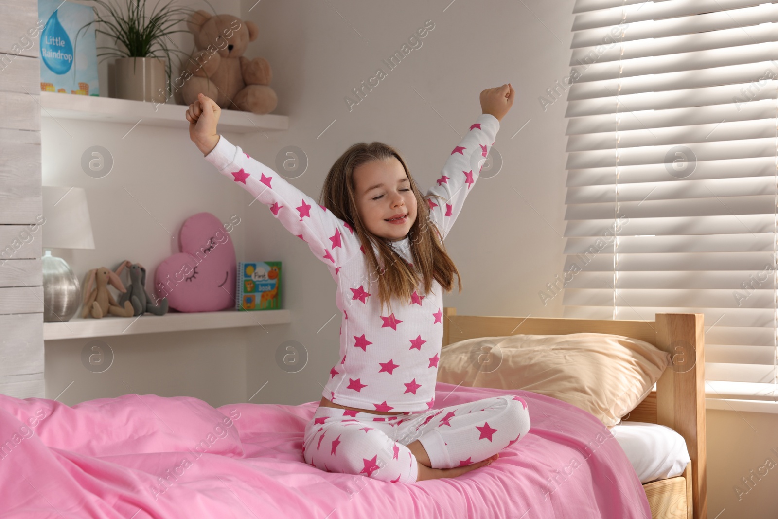 Photo of Cute little girl stretching on bed at home