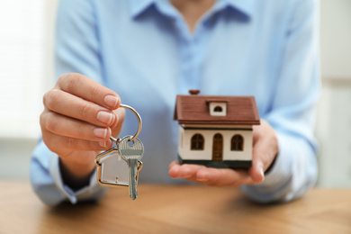 Photo of Real estate agent holding house model and key at wooden table, closeup