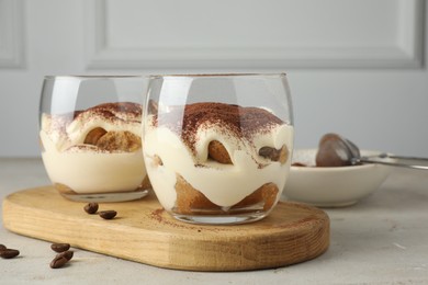 Photo of Delicious tiramisu in glasses and scattered coffee beans on light table