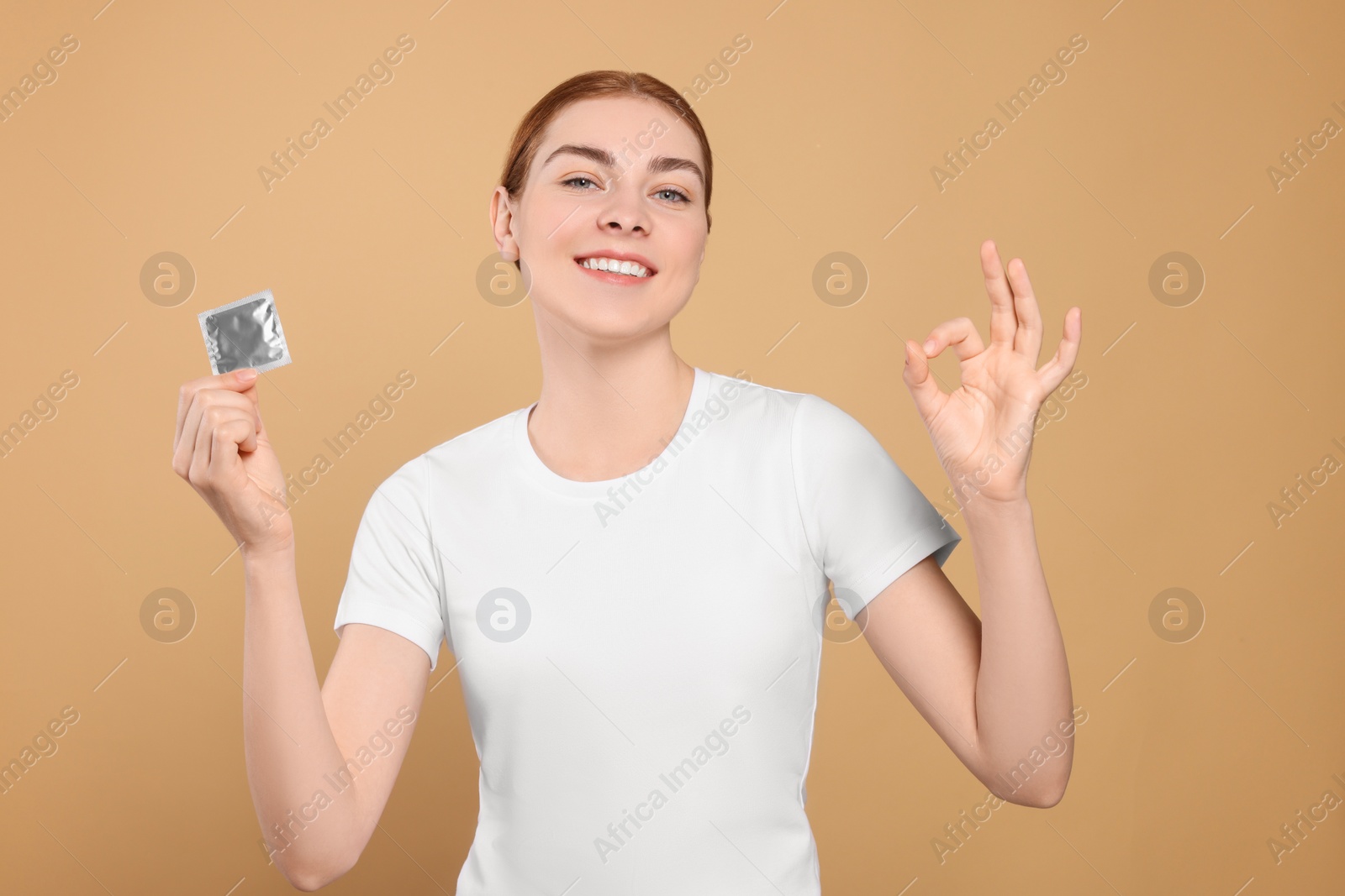 Photo of Woman with condom showing ok gesture on beige background. Safe sex