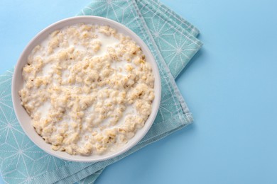 Photo of Tasty boiled oatmeal in bowl on light blue table, top view. Space for text