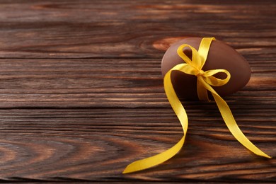 Photo of Tasty chocolate egg with yellow bow on wooden table, space for text