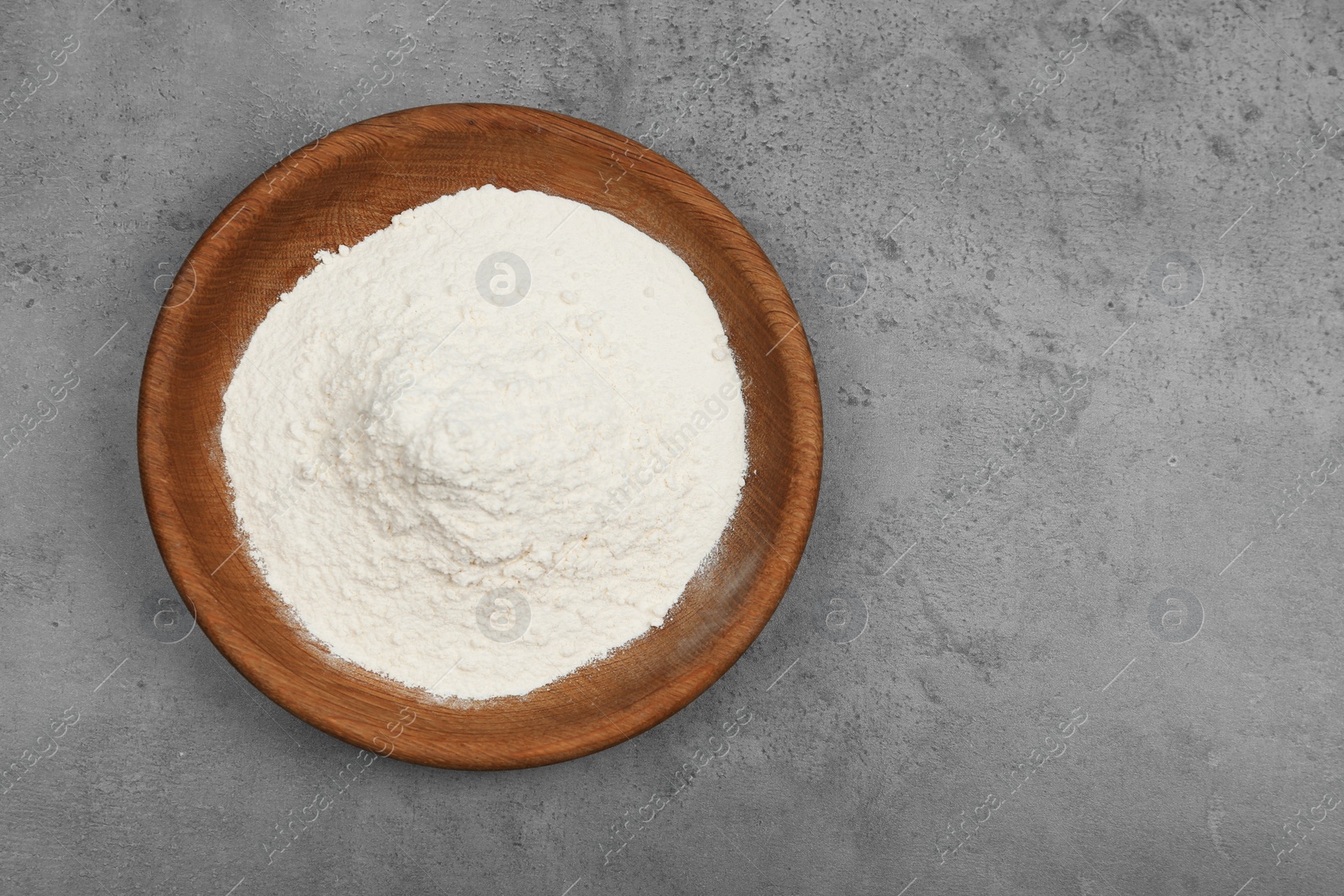 Photo of Wooden bowl with flour on light grey table, top view. Space for text