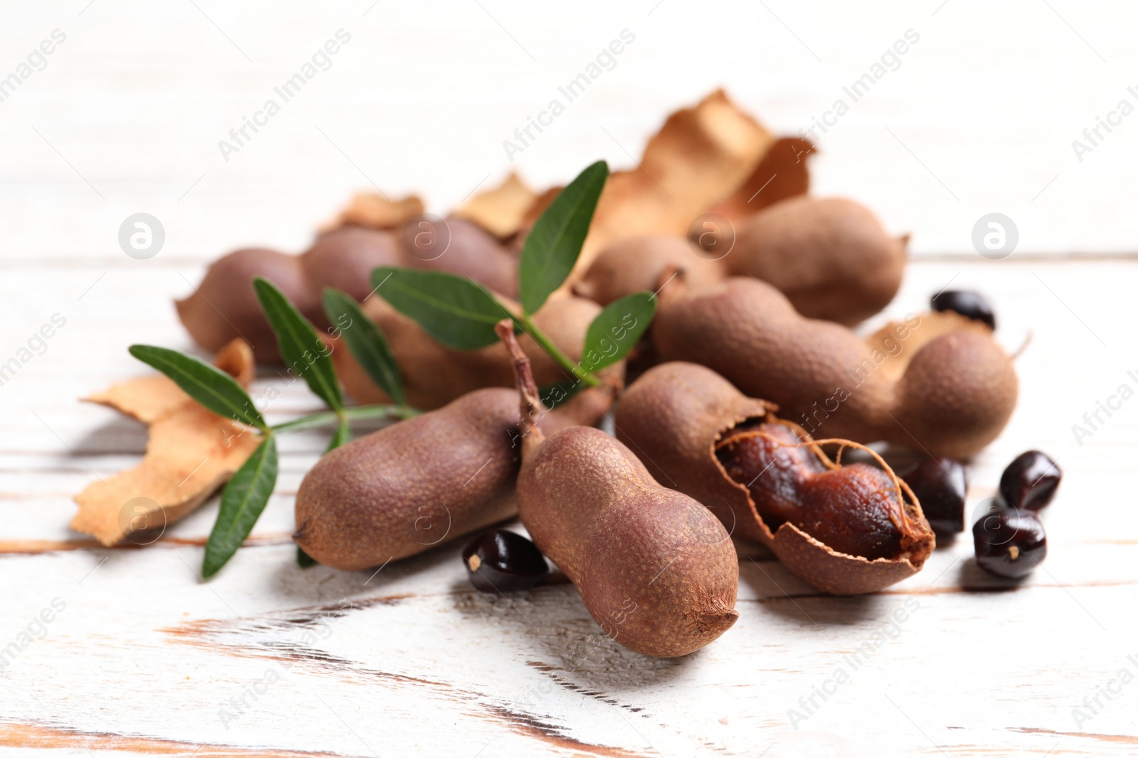 Photo of Delicious ripe tamarinds and leaves on white wooden table, closeup