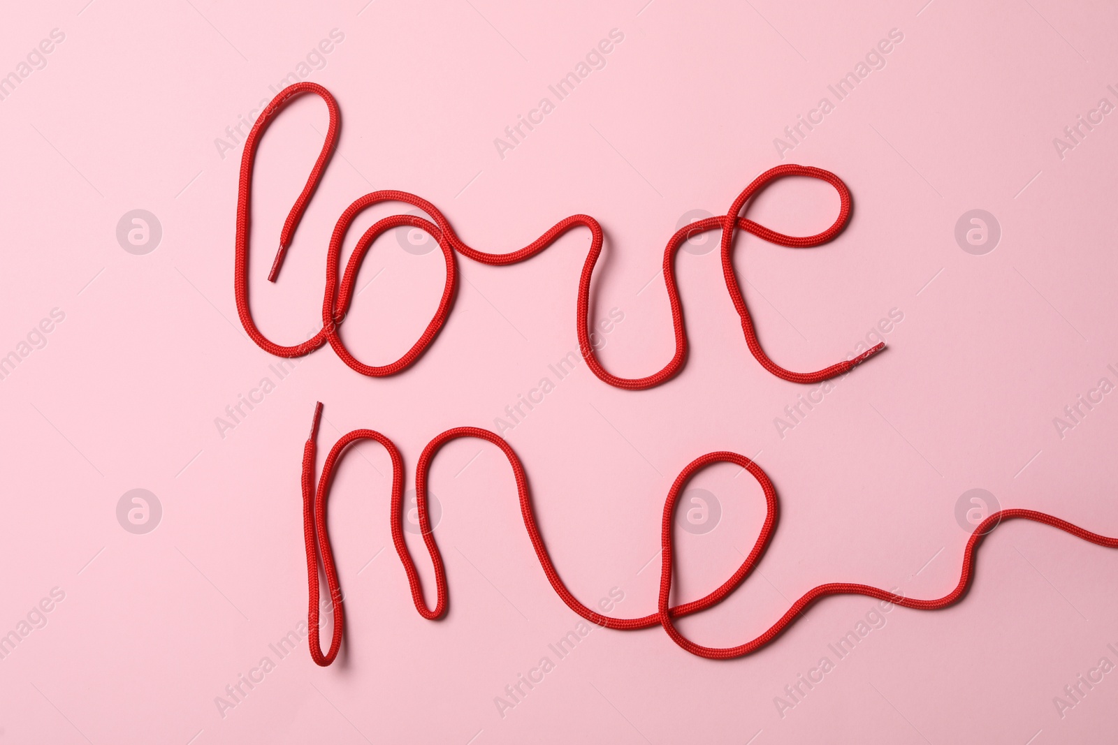 Photo of Phrase Love Me made with red shoe laces on pink background, flat lay