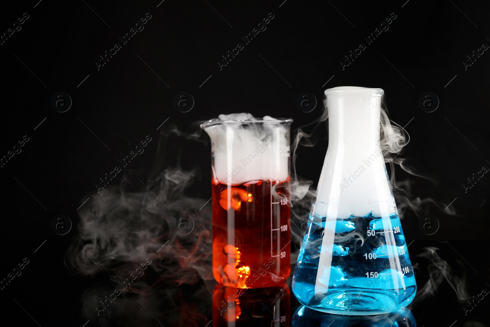 Photo of Laboratory glassware with colorful liquids and steam on black background. Chemical reaction