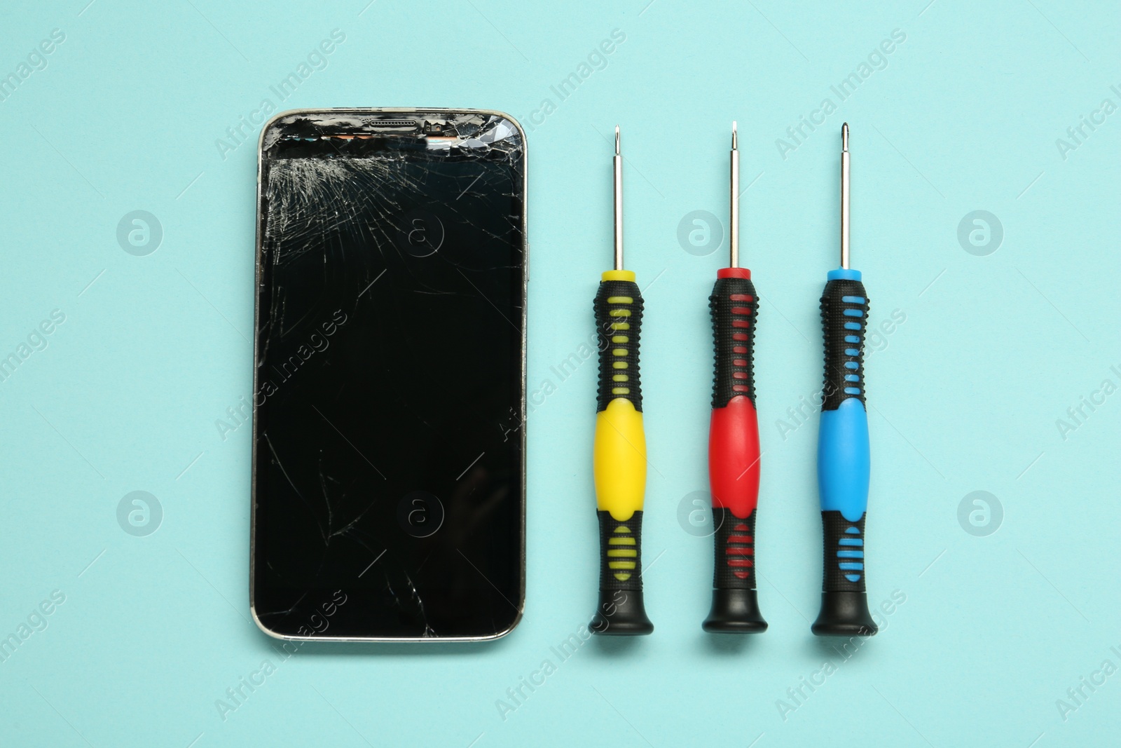 Photo of Damaged smartphone and repair tool set on light blue background, flat lay