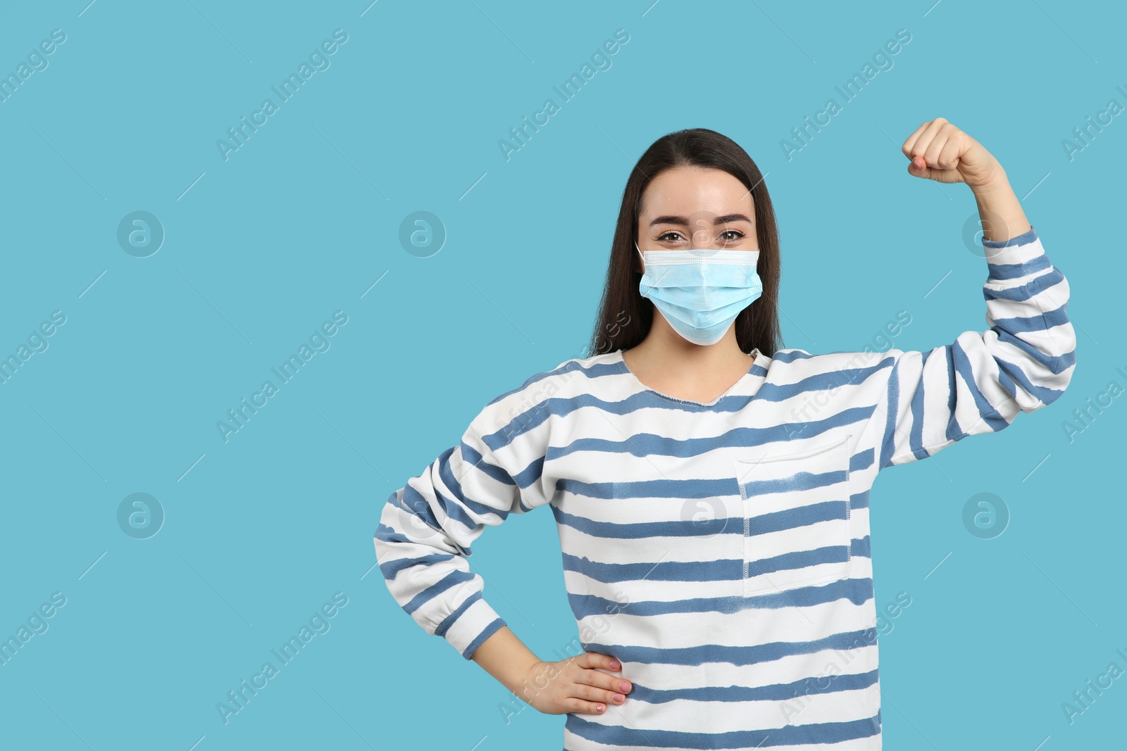 Photo of Woman with protective mask showing muscles on light blue background, space for text. Strong immunity concept