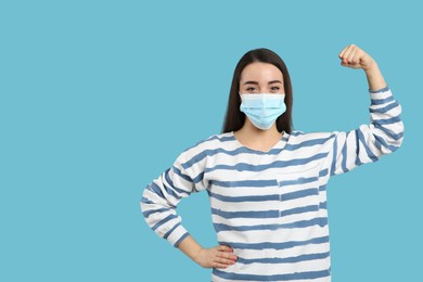 Woman with protective mask showing muscles on light blue background, space for text. Strong immunity concept