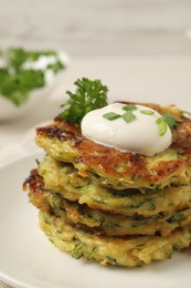 Photo of Delicious zucchini fritters with sour cream on plate, closeup