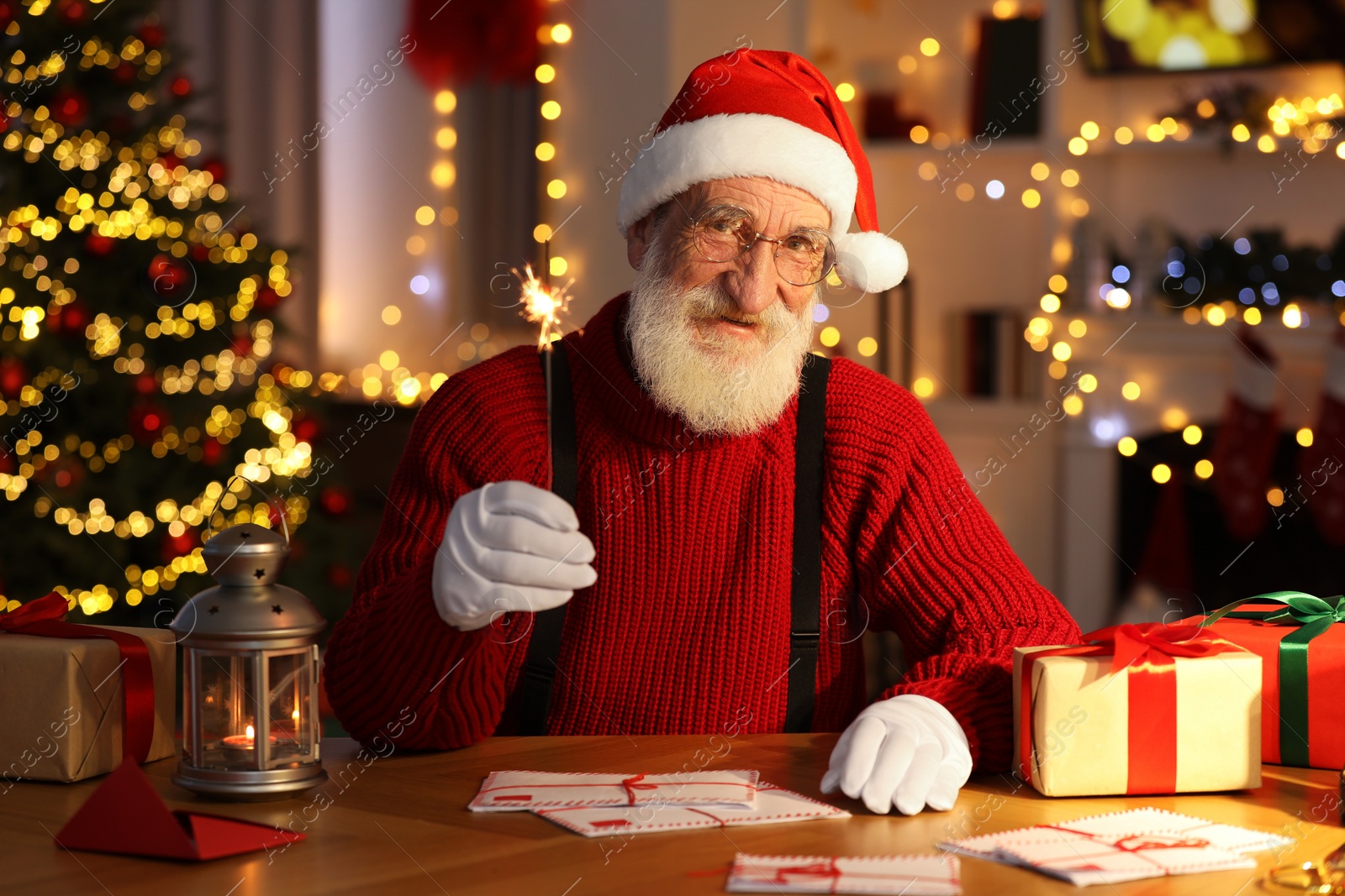 Photo of Santa Claus holding sparkler at his workplace in room with Christmas tree