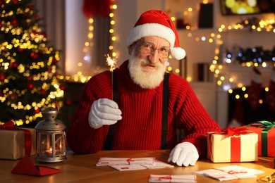 Photo of Santa Claus holding sparkler at his workplace in room with Christmas tree