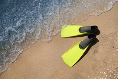 Photo of Pair of yellow flippers on sand near sea, top view. Space for text