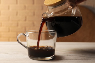 Photo of Pouring coffee into cup at light wooden table, closeup