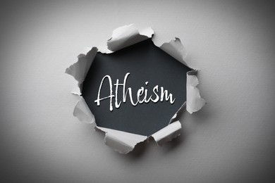 Image of Word Atheism on black background, view through hole in grey paper