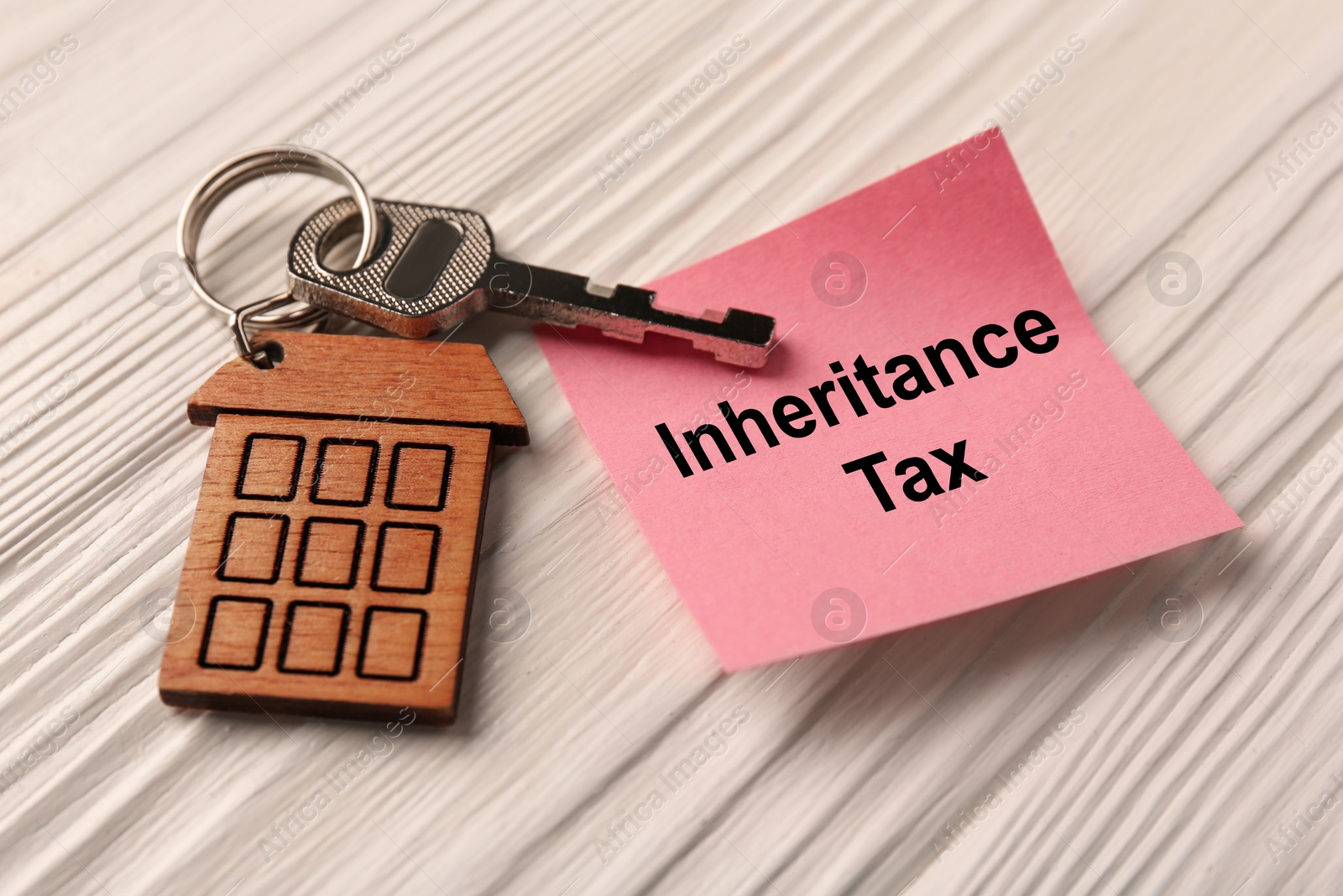 Photo of Inheritance Tax. Paper note and key with key chain in shape of house on white wooden table, closeup