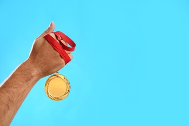 Man holding golden medal on light blue background, closeup. Space for design