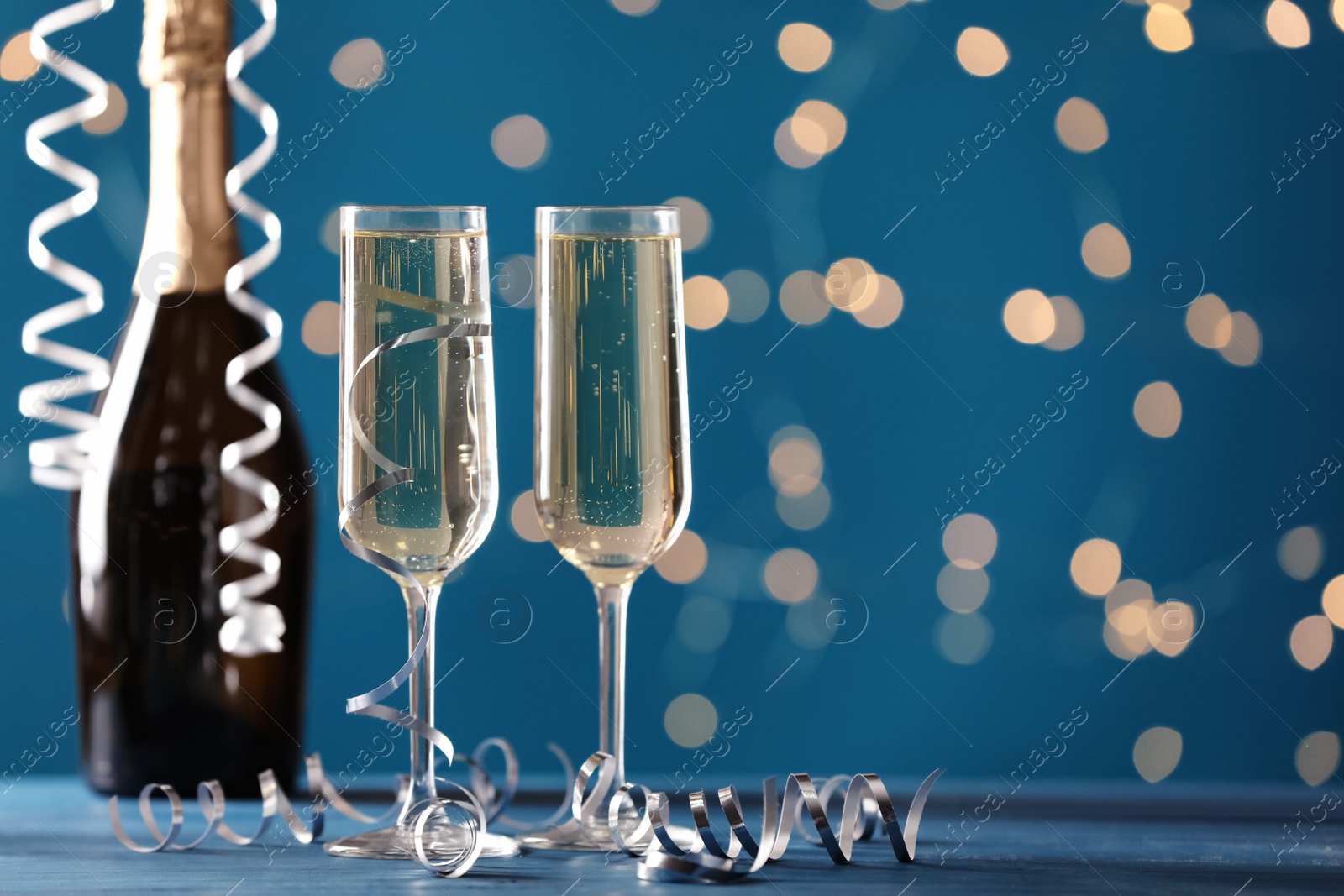 Photo of Glasses and bottle of champagne with serpentine streamers against blurred lights. Space for text