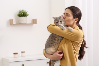 Photo of Young woman kissing her adorable cat at home, space for text