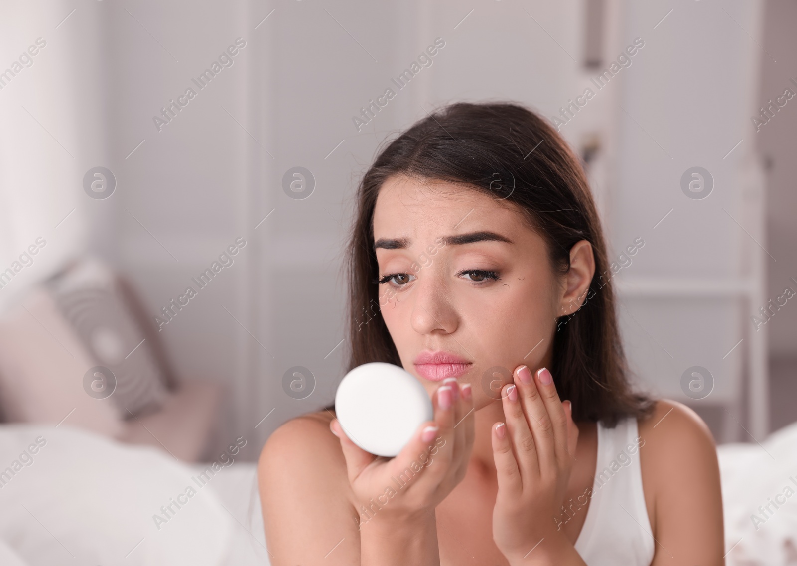 Photo of Young woman with eyelash loss problem looking in mirror indoors