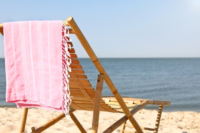 Photo of Empty wooden sunbed and towel on sandy shore. Beach accessories
