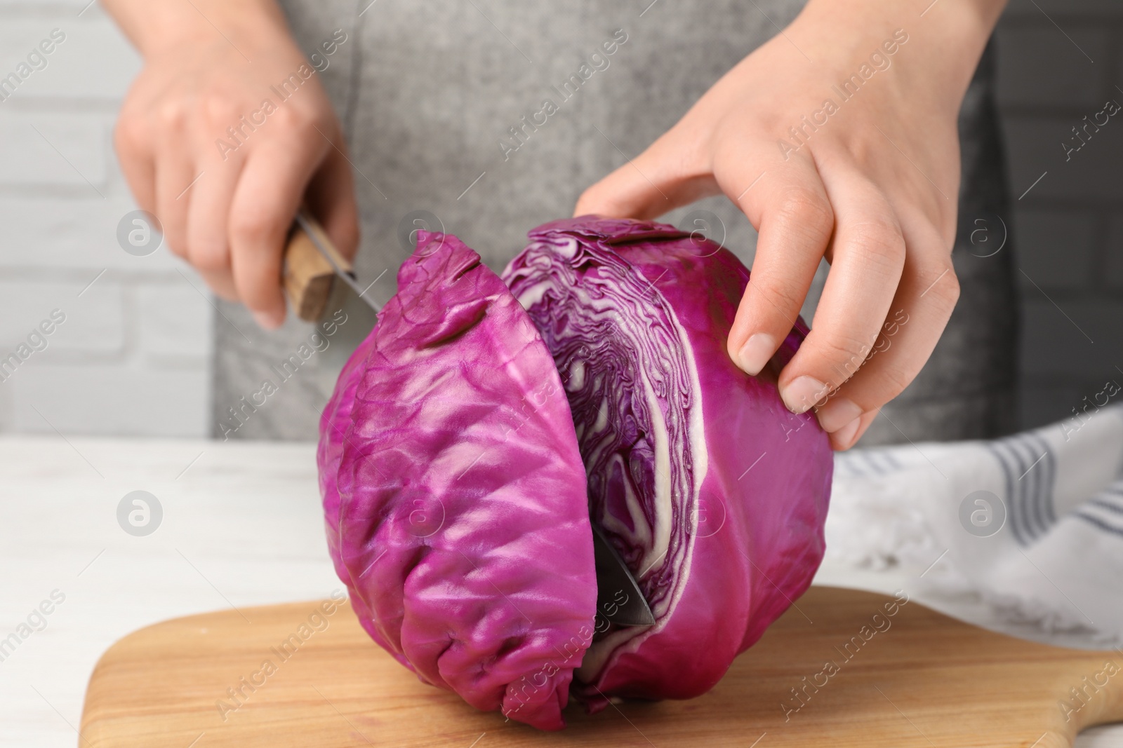 Photo of Woman cutting fresh red cabbage at white wooden table, closeup