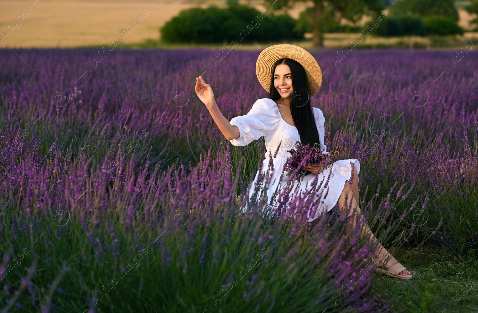 Photo of Beautiful young woman with bouquet sitting in lavender field