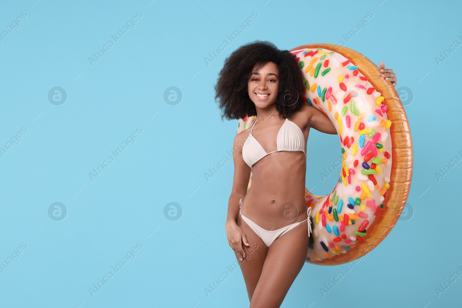 Photo of Beautiful woman in stylish bikini with inflatable ring on light blue background, space for text