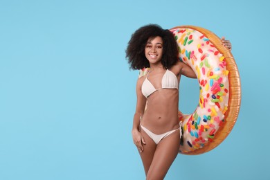 Photo of Beautiful woman in stylish bikini with inflatable ring on light blue background, space for text