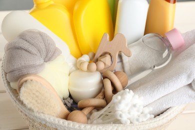 Photo of Wicker basket full of different baby cosmetic products, bathing accessories and toys on table, closeup